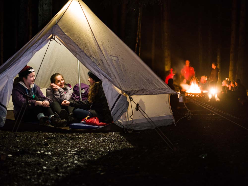 three female cubs in a tent with a campire outside
